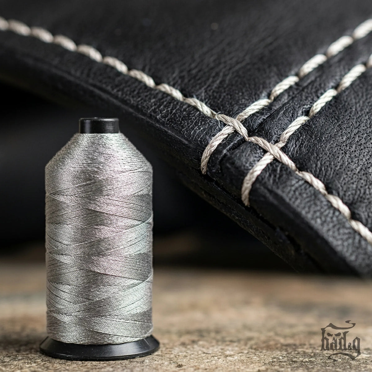 Spool of silver thread next to a black leather product with silver stitching