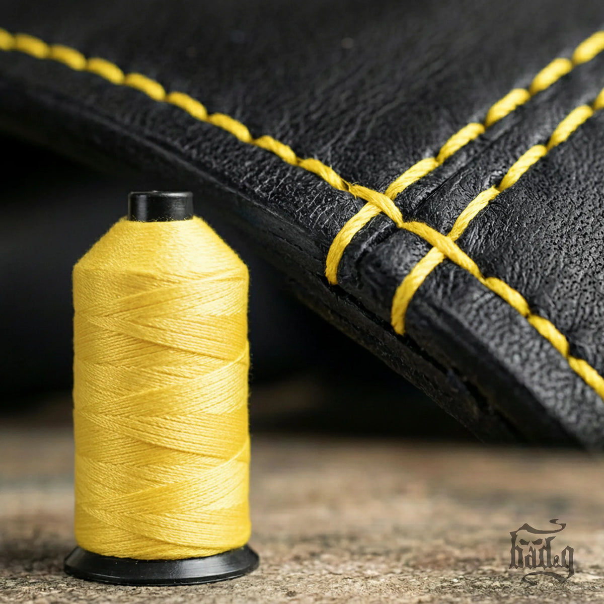 Spool of yellow thread next to black leather with yellow stitching