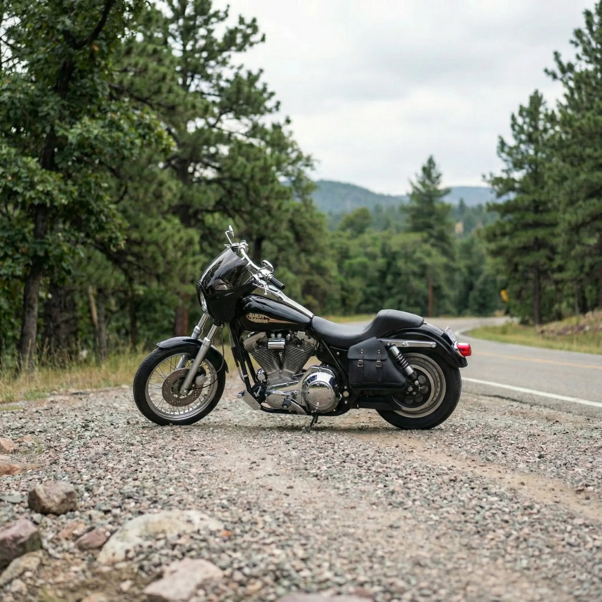 Black motorcycle on a gravel road with trees and mountains in the background