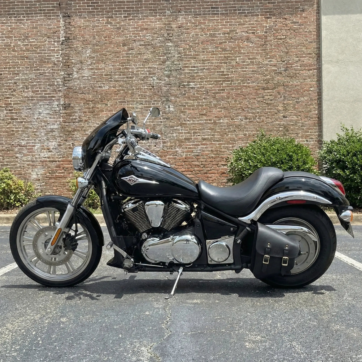 Black Kawasaki Vulcan motorcycle parked in a parking lot with a brick wall background.